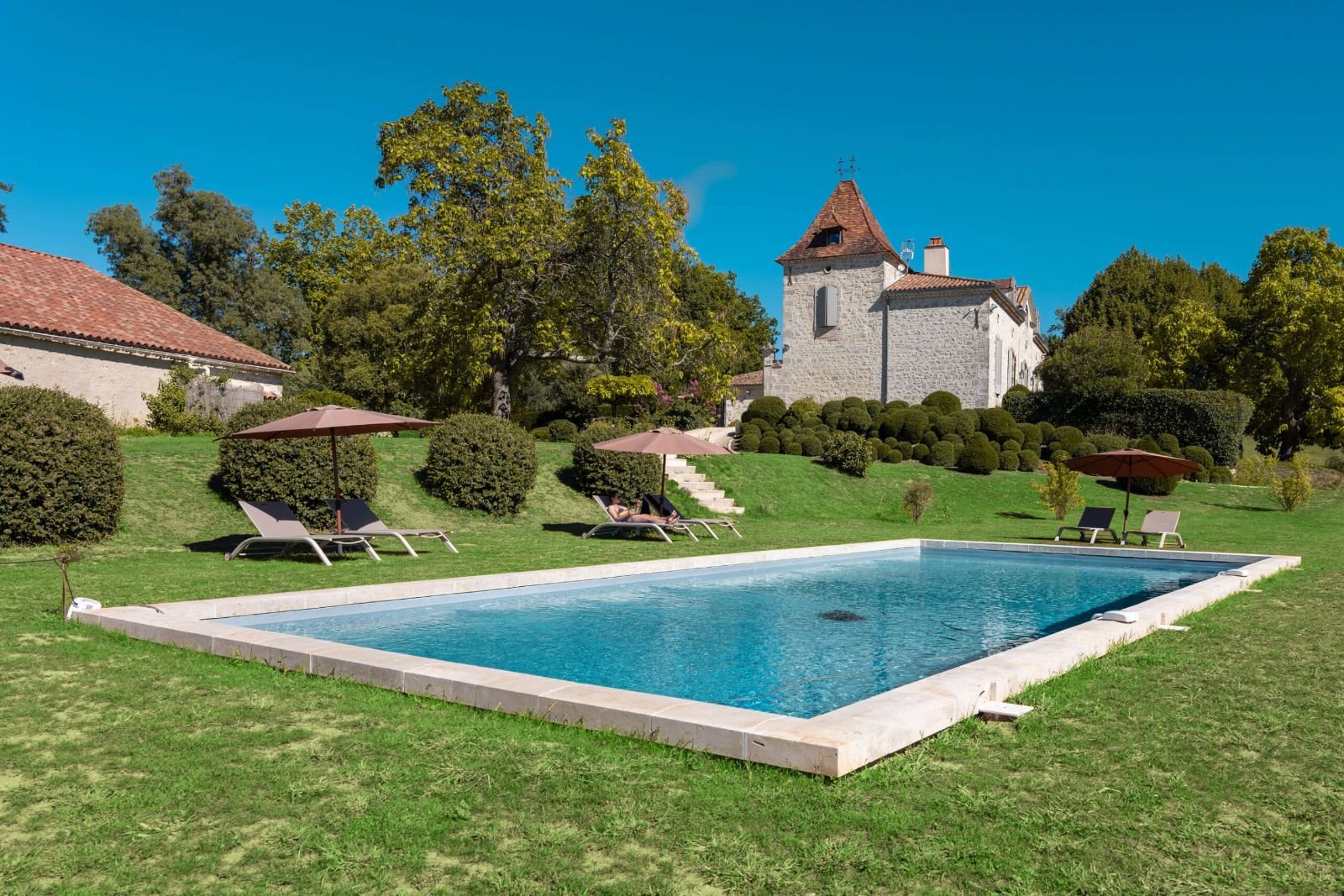 La piscine du manoir et ses transats sur la pelouse, la tour en arrière-plan